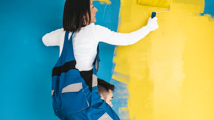 Happy couple renovating their home. They are together painting a wall in blue or teal and yellow colors.